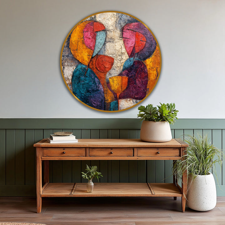 Softly colored hues blend in this abstract oil painting artwork depicting figures sharing a drink, encased in a golden circular frame above a wooden console table.