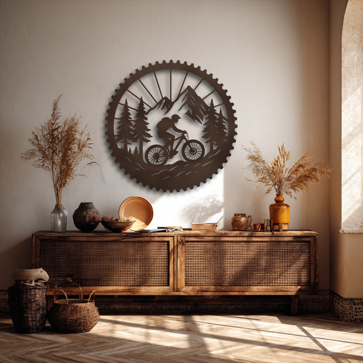 A vertically oriented circular metal art for wall featuring a mountain biker's silhouette amidst a rugged forest and towering mountains.