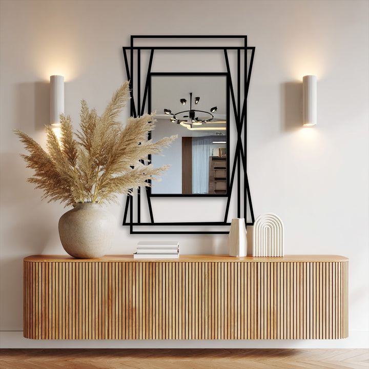 Foregrounded by pampas grass in a stoneware vase atop a streamlined cabinet, a layered symmetrical angular framed wall mirror presents modern metal geometry, offering subtle home decoration.