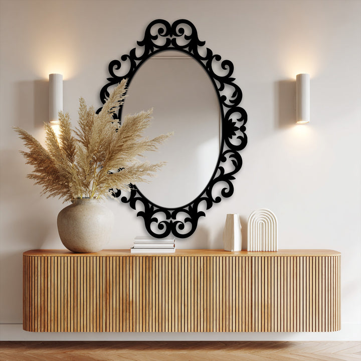 Bathed in light, a black ornate scroll oval framed wall mirror reflects its surroundings.