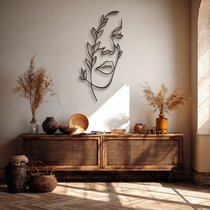 The organic forms of a minimalist female face with botanical elements in this decorative metal art piece are subtly illuminated.