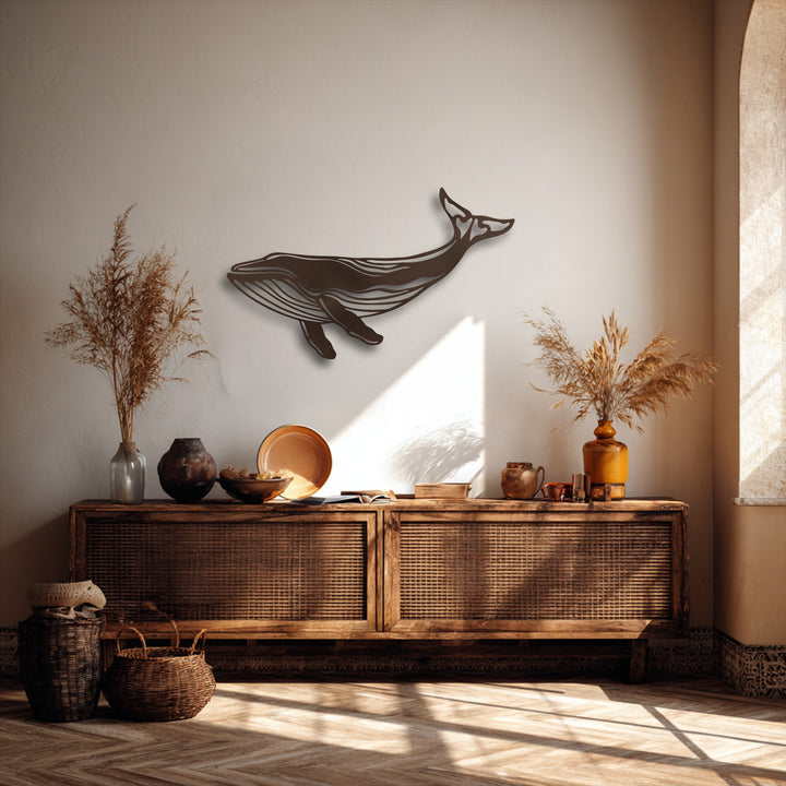 A textured, light-toned wall serves as a serene backdrop for the majestic whale silhouette metal artwork, bathed in sunlight from an arched window.