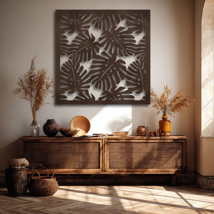 The striking transition from light wall background to deep brown tropical monstera leaf pattern in this metal wall decor creates depth.