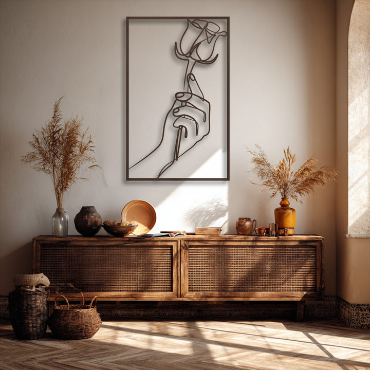 Highlighting organic forms, a unique metal wall art piece depicts an elegant minimalist hand holding a delicate rose line art.