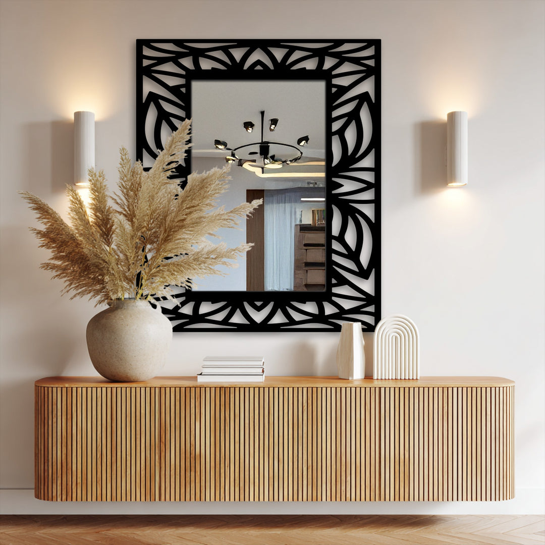 Highlighting the realistic detail, a decorative framed wall mirror reflects a modern room, showcasing its tropical leaf silhouette and black metal artwork design mounted above a wooden cabinet.