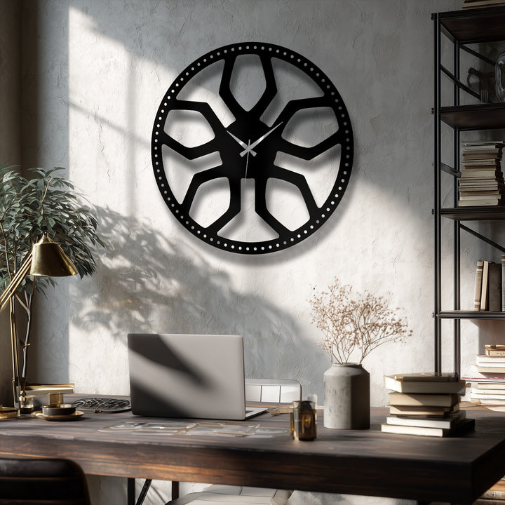 Deep black abstract radial pattern metal artwork clock with a modern geometric design on a textured light gray wall.