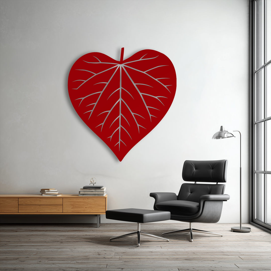 A striking red heart-shaped leaf silhouette metal artwork with intricate vein details commands attention on a white wall.