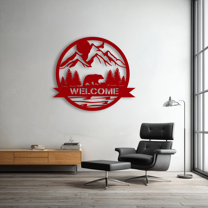 A sleek black leather armchair and ottoman sit in the foreground, complementing the striking red Mountain Bear Welcome Sign metal artwork on the wall.