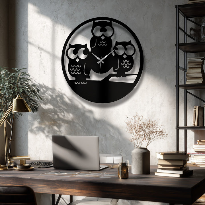 The darkest area highlights the bold Three Owls Silhouette Metal Wall Clock, a prominent metal artwork piece against the rich, dark wooden desk.