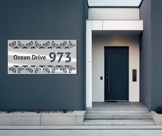 Negative space highlights the butterfly patterns surrounding the 'Ocean Drive 973' of this unique metal wall art address sign.