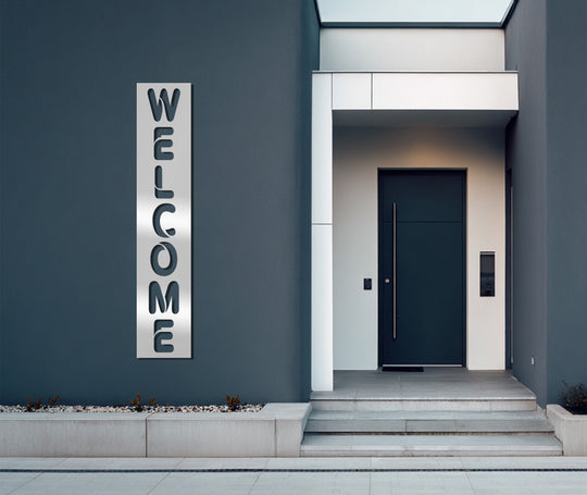 Foreground details feature a modern welcome sign rendered as distinctive metal artwork set against the sleek facade of a contemporary entryway.