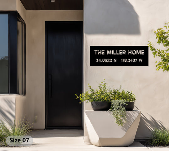 The neutral textured background highlights the modern black metal artwork sign displaying a custom name and coordinates, offering a sleek contrast.