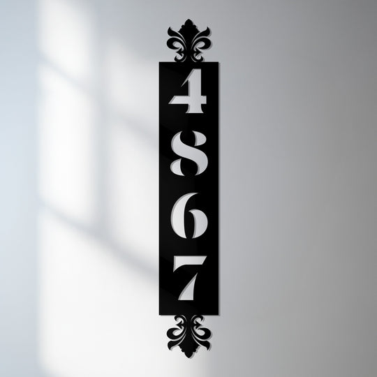 Black vertical metal art for wall address sign features decorative fleur-de-lis accents framing cutout house numbers 4867 against a light gray background.