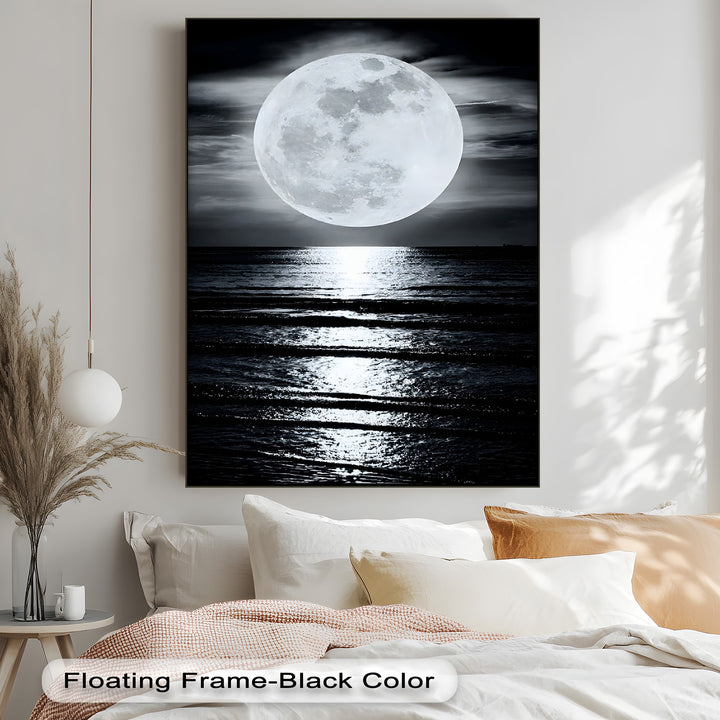 Plush white pillows and a soft, textured blanket provide a cozy foreground for the serene moonlit ocean reflection hanging canvas.