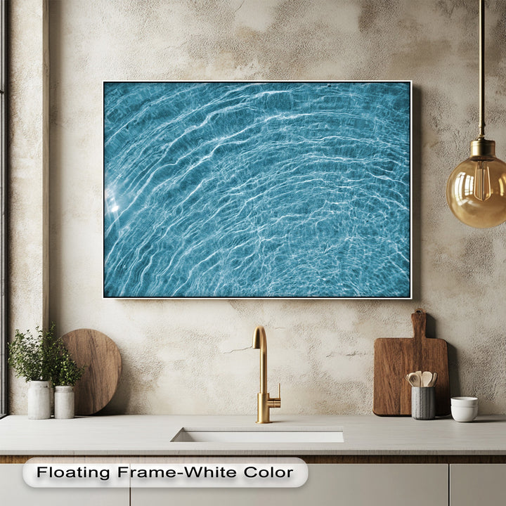 Warm-toned textured walls, a golden faucet, and stylish kitchen items artfully frame the vibrant blue water ripple canvas wall art.