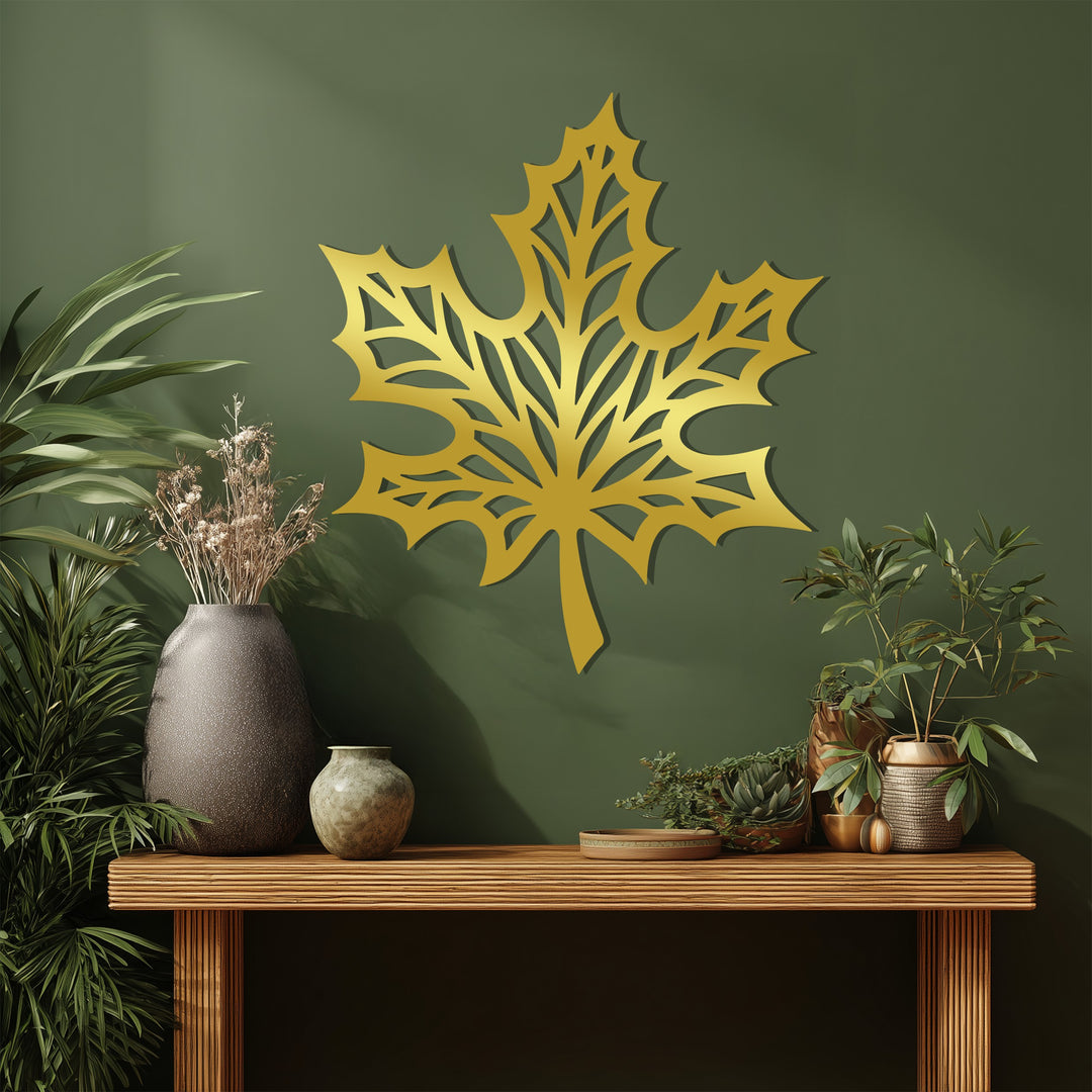 Contrasting textures highlight the smooth, golden surface of the maple leaf metal artwork against the matte green wall, enhancing its nature-inspired design.