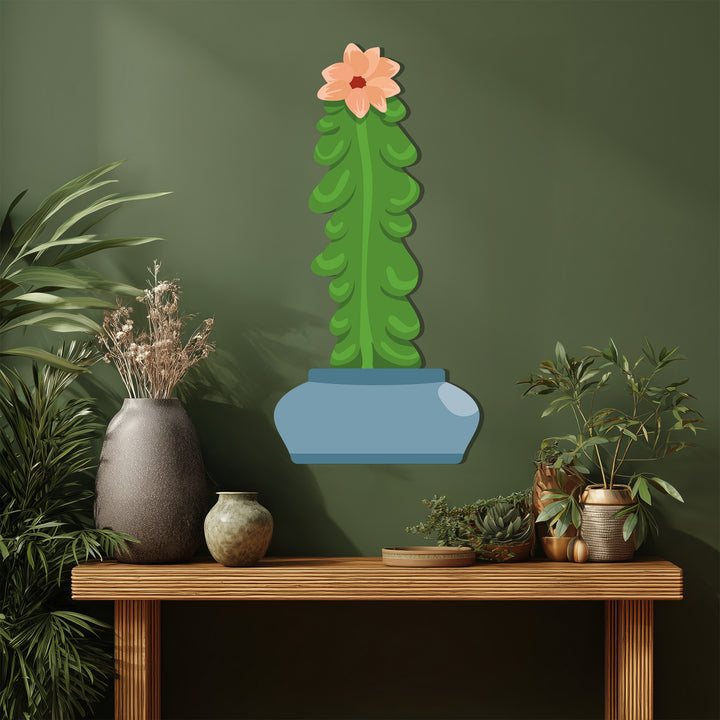 The negative space highlights the stylized column cactus in this unique metal wall art, mounted against a sage green backdrop with a console table and plants below.