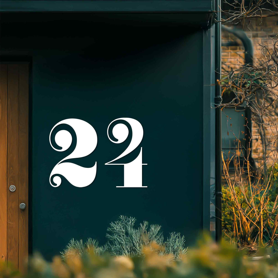 Bold white metal house numbers sharply contrast with the deep teal surface in this display of vintage style metal wall decor.