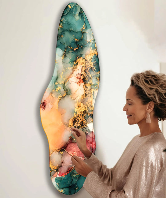 A woman admires an irregular asymmetrical green marble glass print wall art with gold accents and warm orange hues.