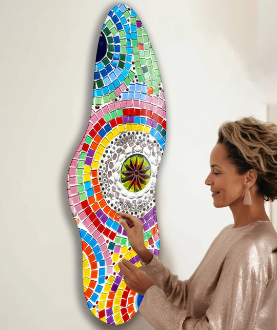 A woman in a shimmering dress is about to touch a vibrant, abstract glass wall art print, with ample negative space on the wall.