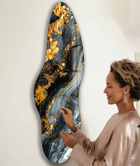 A woman admires the interplay of light and shadow on a striking gold marble glass wall artwork, highlighting its deep blacks and shimmering gold flecks.