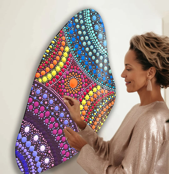 A woman admires a vibrant, irregular mosaic-style glass wall art piece, showcasing intricate dot patterns in purple, blue, and rainbow hues, representing the best glass art.
