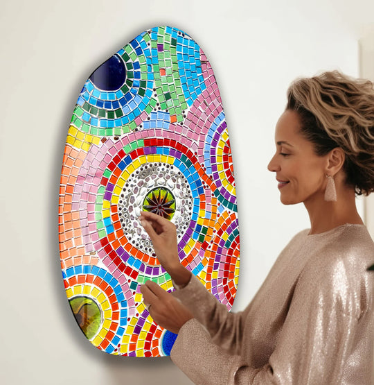 A woman's hand delicately touches the shimmering mosaic surface of a vibrant, asymmetrical glass wall art decor.