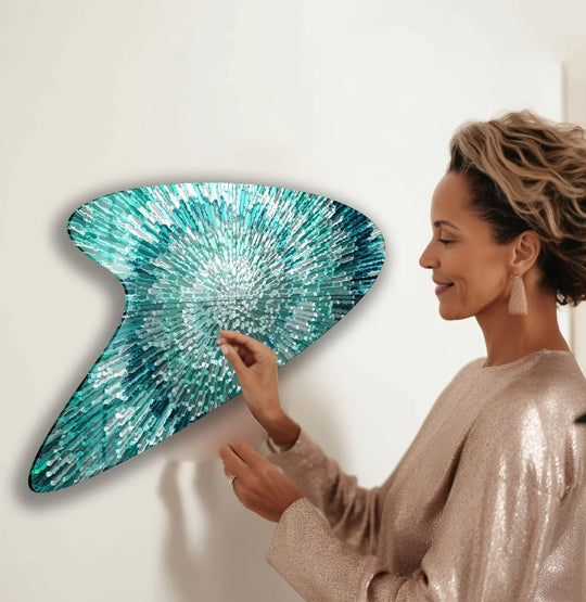 A woman in a sequined dress admires abstract turquoise line glass wall art, its radiant pattern filling the surrounding negative space.