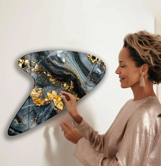 A modern gold marble glass wall art piece with a textured, swirling black and gray surface accented with shimmering gold leaf flakes.