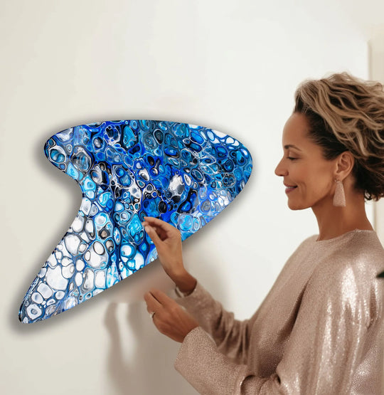 A woman hangs an abstract, swirling blue marbled glass decorative wall art with a glossy, enameled finish.