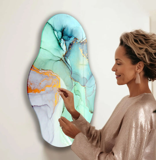 A woman in a sequined dress admires a large, irregular oval abstract turquoise glass wall art piece with gold accents.
