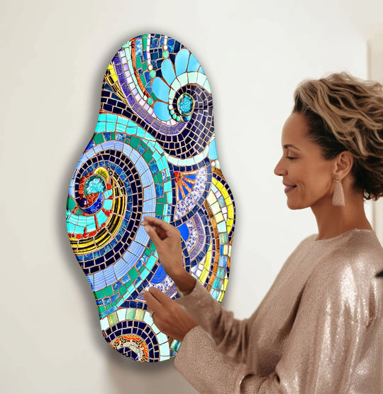 A woman admires a colorful, oval-shaped glass wall art with dominant shades of blue, teal, and purple, featuring intricate mosaic patterns, making it a stunning piece of best glass art.