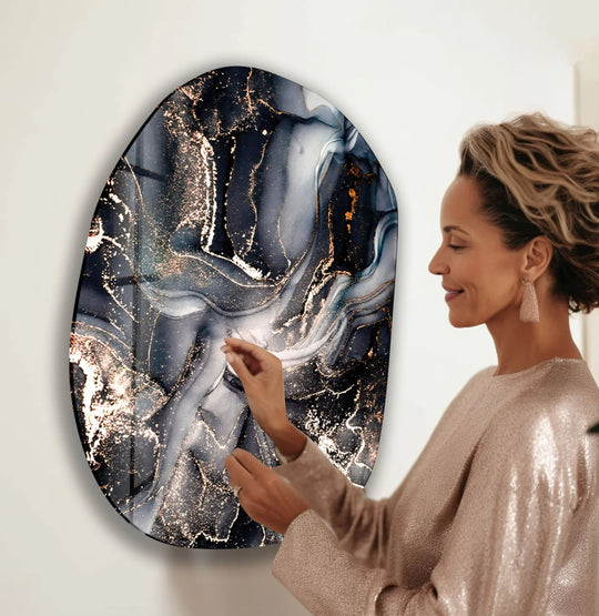 A contemporary oval glass wall art print features striking geometric patterns in swirling black, gray, and shimmering gold ink textures.