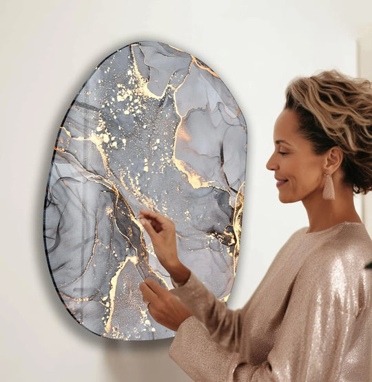 Intricate layers of grey and gold watercolor create depth on this oval print wall art, echoing the woman's reflective gaze.