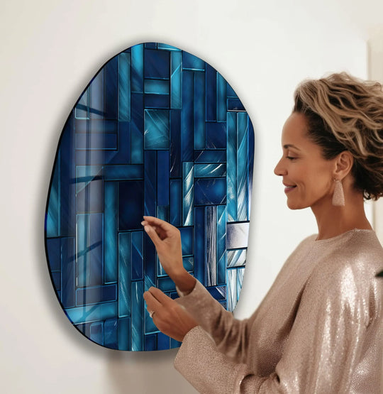 A woman in a shimmering gold top admires a detailed, abstract navy blue oval glass wall art print with a textured, mosaic-like design.