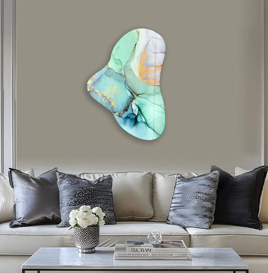 A shimmering turquoise alcohol ink asymmetrical glass art painting on a wall above a white couch with decorative pillows and a coffee table.