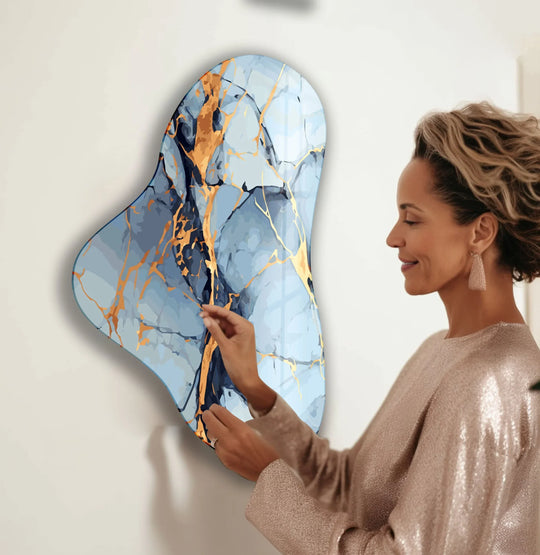 A woman admires the elegant mood of abstract blue marble glass wall art with gold accents.