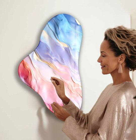 A woman admires a soft pink and blue abstract glass print wall art with flowing lines and a translucent quality.