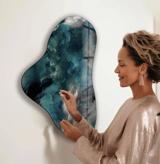 A woman admires a bright, abstract glass art painting featuring swirling turquoise and white tones.