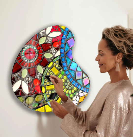 A woman admires a colorful, irregularly shaped glass printing piece on a plain white wall.