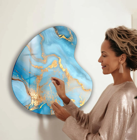 A woman admires a glass art painting where deep sapphire blues smoothly transition into shimmering gold accents.