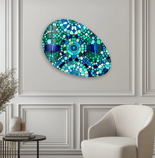 An oval-shaped mosaic glass art piece displays vibrant blue and green geometric patterns and abstract designs.