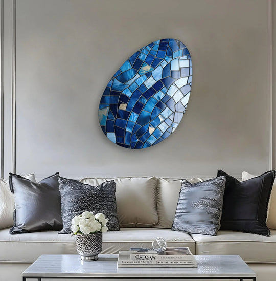 An oval mosaic glass wall art with sapphire and azure blues forms a focal point above a neutral sofa.