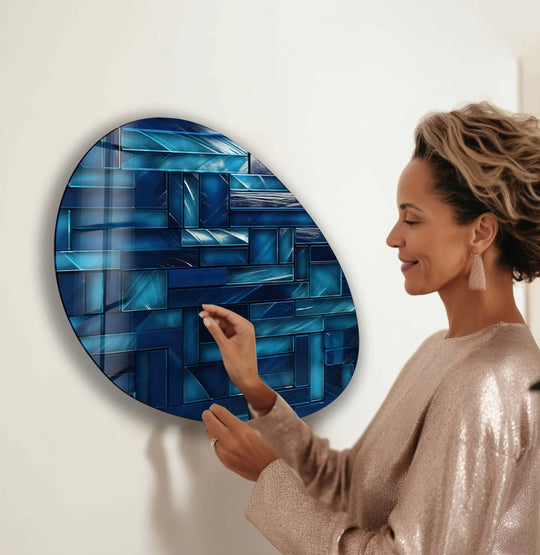 A woman in a sequined top adjusts a stunning navy blue mosaic glass wall art with a shimmering effect.