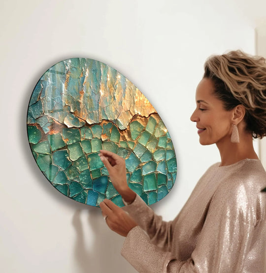 A woman admires a green and gold abstract oval glass wall artwork, capturing a moment of serene contemplation.