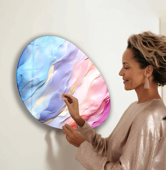A woman admires abstract oval glass wall art where light and shadow create swirling pink and blue patterns, enhancing the home decor.