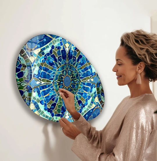 A woman admires the highly saturated blues and greens of this unique oval glass wall art print with intricate mosaic patterns.