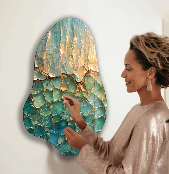 An abstract, irregularly shaped glass art painting in shades of turquoise and gold hangs vertically.