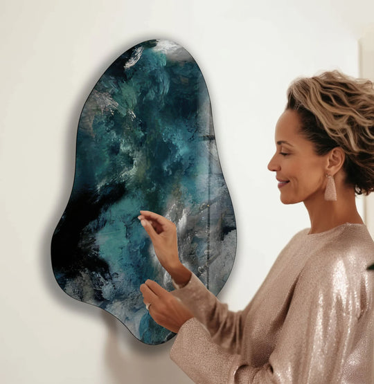 A woman admires a dark, moody abstract glass wall art with deep blues and black tones.