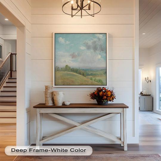 Warm color temperature illuminates the modern oil painting art of a vintage landscape with rolling hills, framed in white, above a rustic console table.